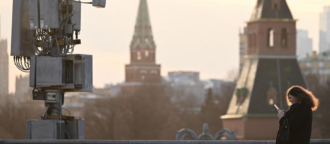 Eine Frau nutzt ihr Smartphone auf der Moskvoretsky-Brücke an einem Mobilfunkmast im Zentrum von Moskau, Russland.