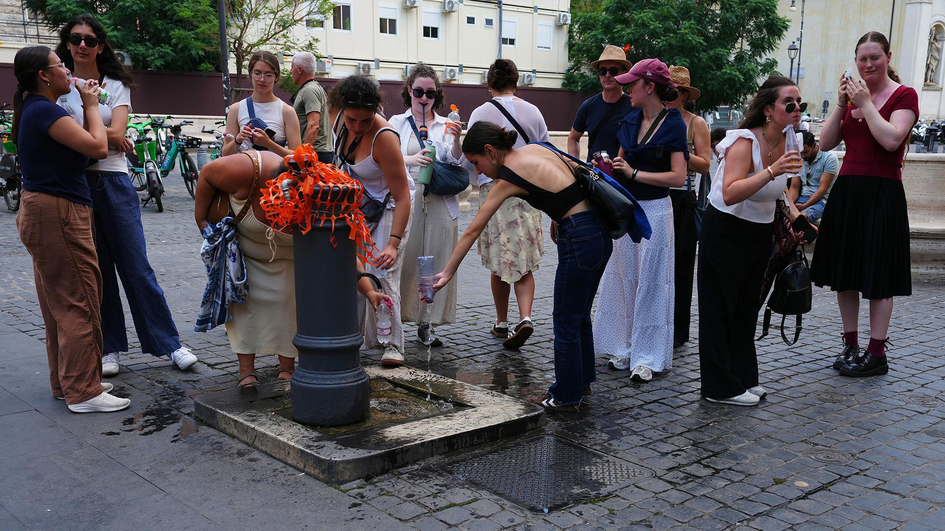 Menschen füllen an einem Brunnen Wasserflaschen. | Alessandra Tarantino/AP/dpa