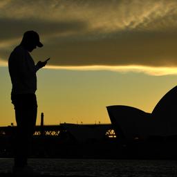 Ein Mann steht vor dem Opernhaus in Sydney und blickt auf sein Mobiltelefon. (Archivbild vom 26.07.2021)