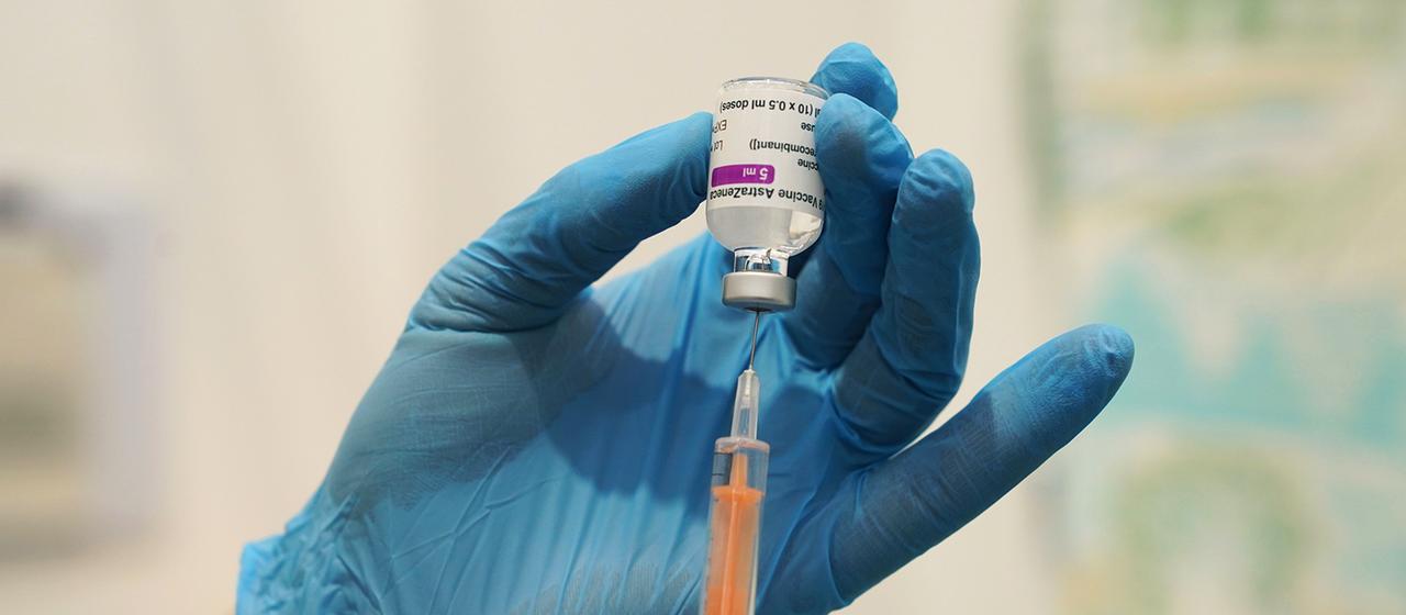 Eine Spritze wird aus einer Ampulle, auf der "AstraZeneca" steht, befüllt.