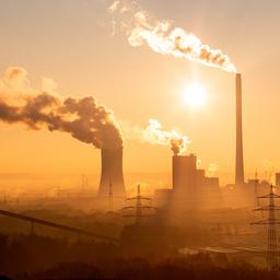Die Sonne geht über Schornsteinen und einem Kühlturm eines Kraftwerks auf