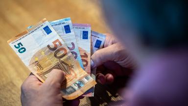 Ein älterer Mann sitzt an einem Tisch und zählt Geld.