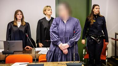 Andrea Tandler steht in einem Gerichtssaal vor ihren Verteidigerinnen und einer Justizbeamtin. 