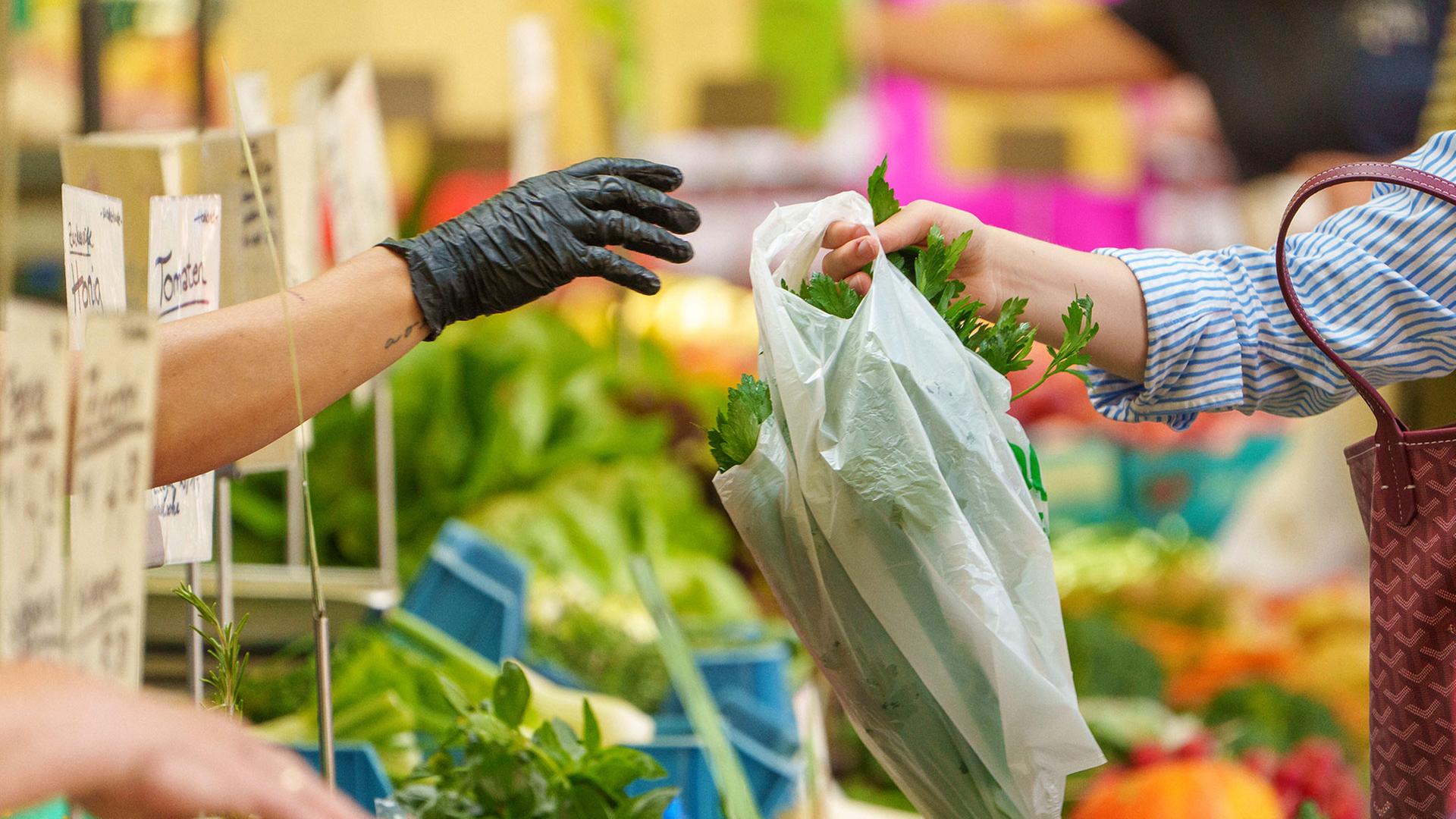 Auf dem Wochenmarkt wird eine Tüte zum Kunden gereicht.  | picture alliance/dpa