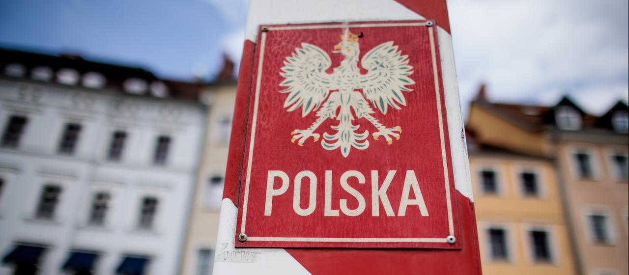 Ein polnischer Grenzpfosten steht vor Restaurants neben der Straße und dem Ufer der Neiße