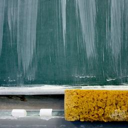 Eine Schultafel, darunter ein Schwamm und Kreide. 