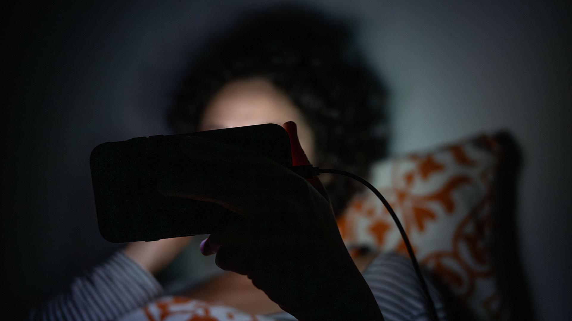 Eine Person liegt im Bett und guckt in ihr Smartphone. | picture alliance/dpa