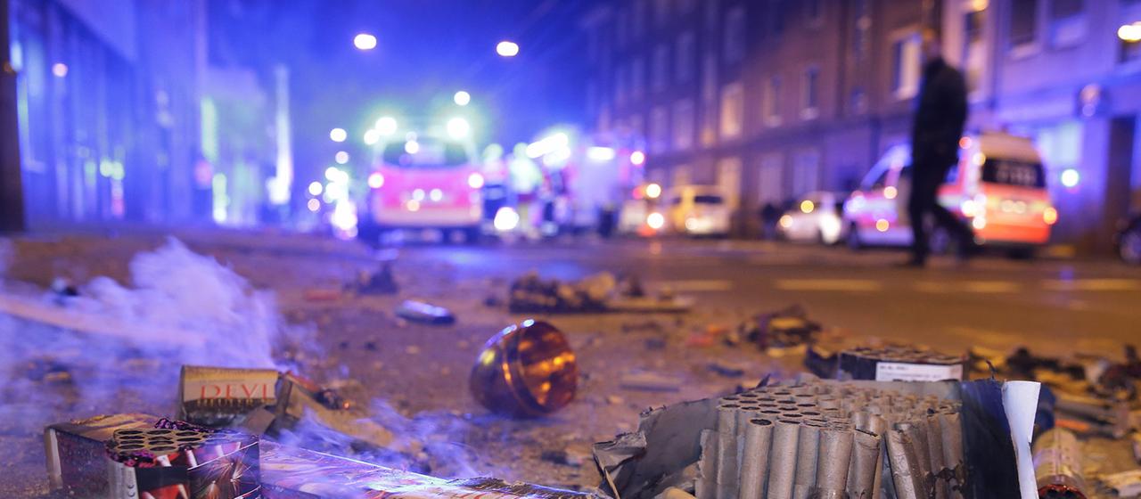 Abgebrannte Böller liegen nach der Silvesternacht auf der Straße im Hintergrund sind Feurwehrfahrzeuge zu sehen.