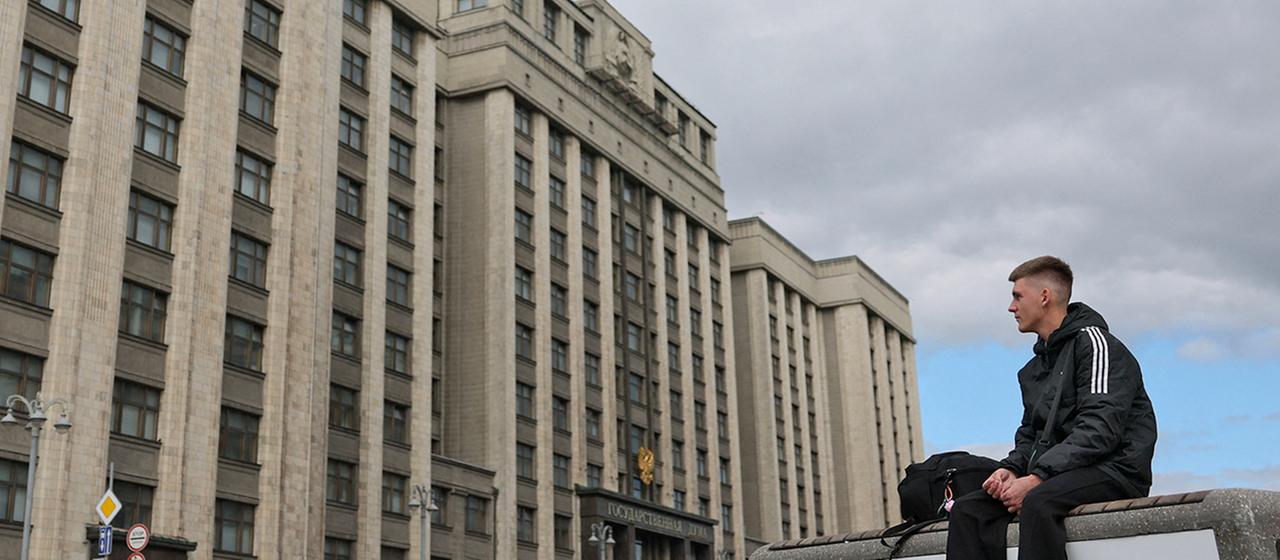 Ein junger Mann sitzt auf einer Bank vor dem Hauptsitz des Unterhauses des russischen Parlaments, der Staatsduma, in Moskau, Russland