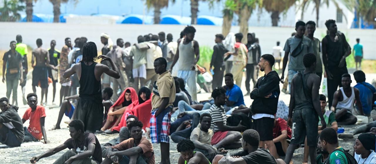 Menschen am Strand warten darauf, ein Center für Kurzzeit-Migration zu betreten.