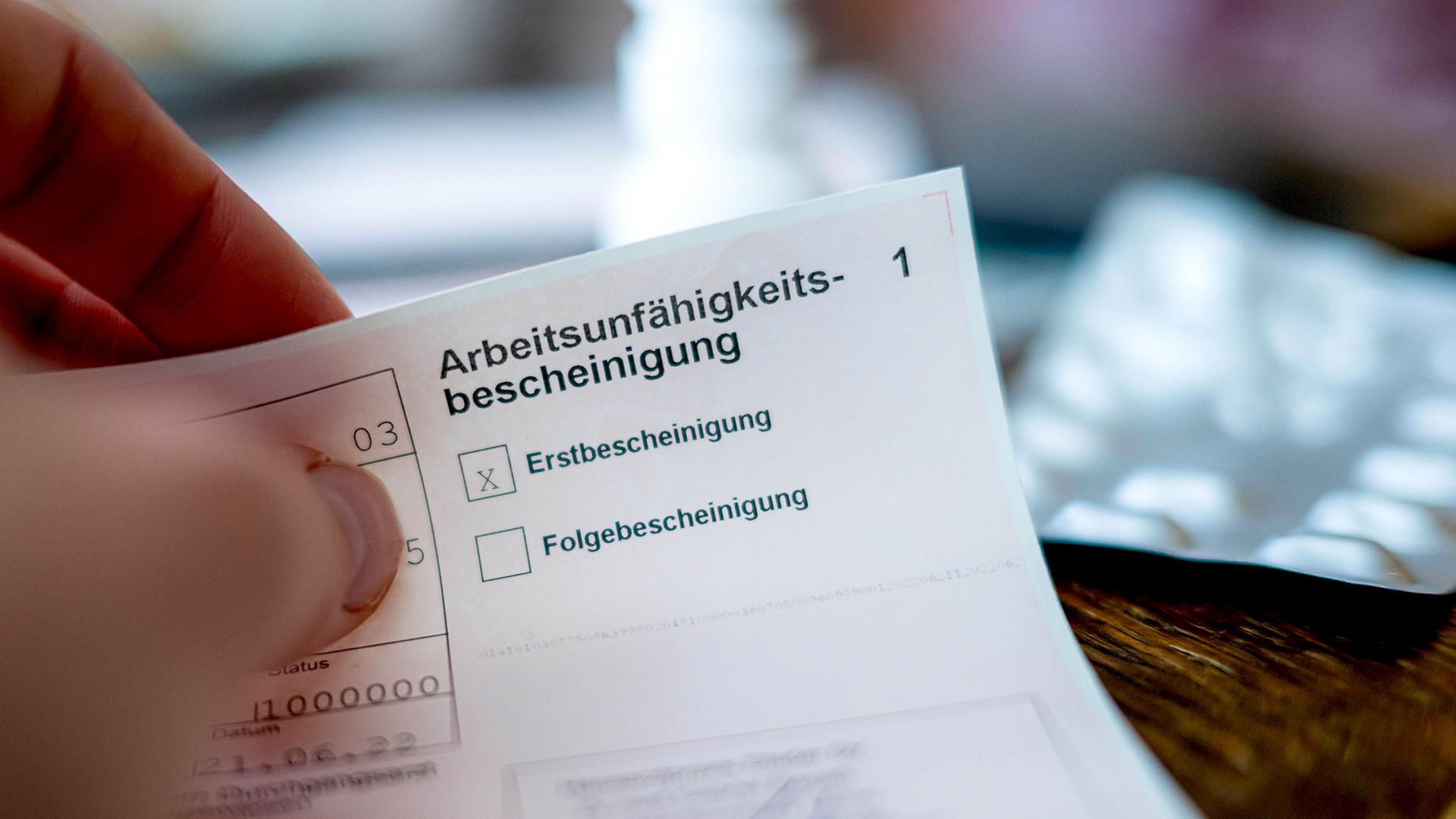 Eine Person hält eine ausgefüllte Arbeitsunfähigkeitsbescheinigung in der Hand. | Sina Schuldt/dpa