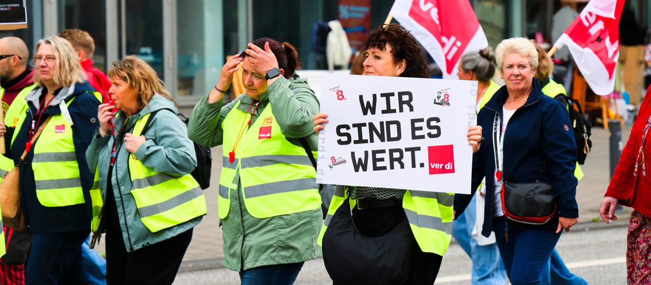 Männer und Frauen in gelben Westen halten Plakate und ver.di-Flaggen