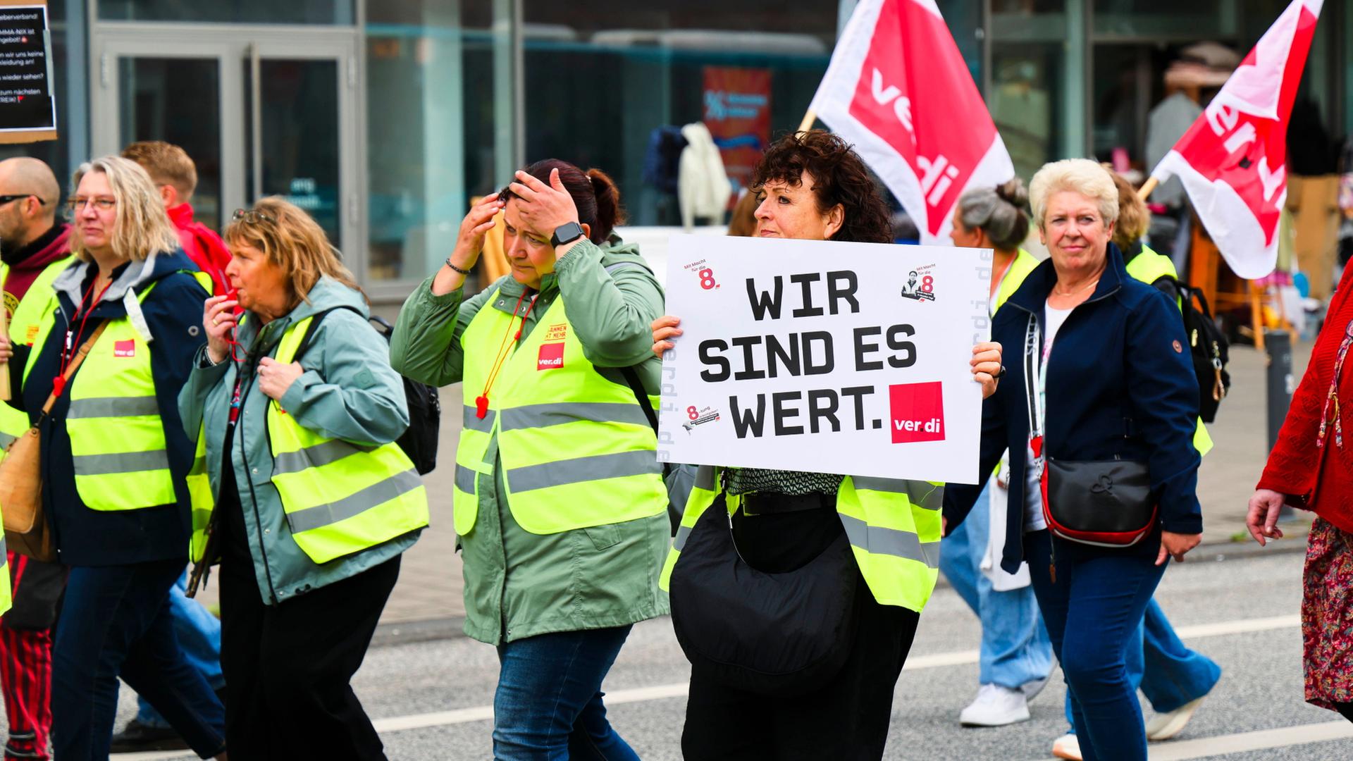Männer und Frauen in gelben Westen halten Plakate und ver.di-Flaggen | Frank Molter/dpa