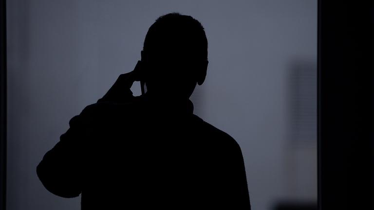Die Silhouette eines Mannes, der mit einem Smartphone telefoniert.