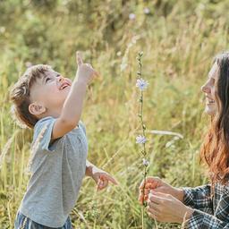 Mutter und Sohn spielen mit Blumen auf einem Feld.