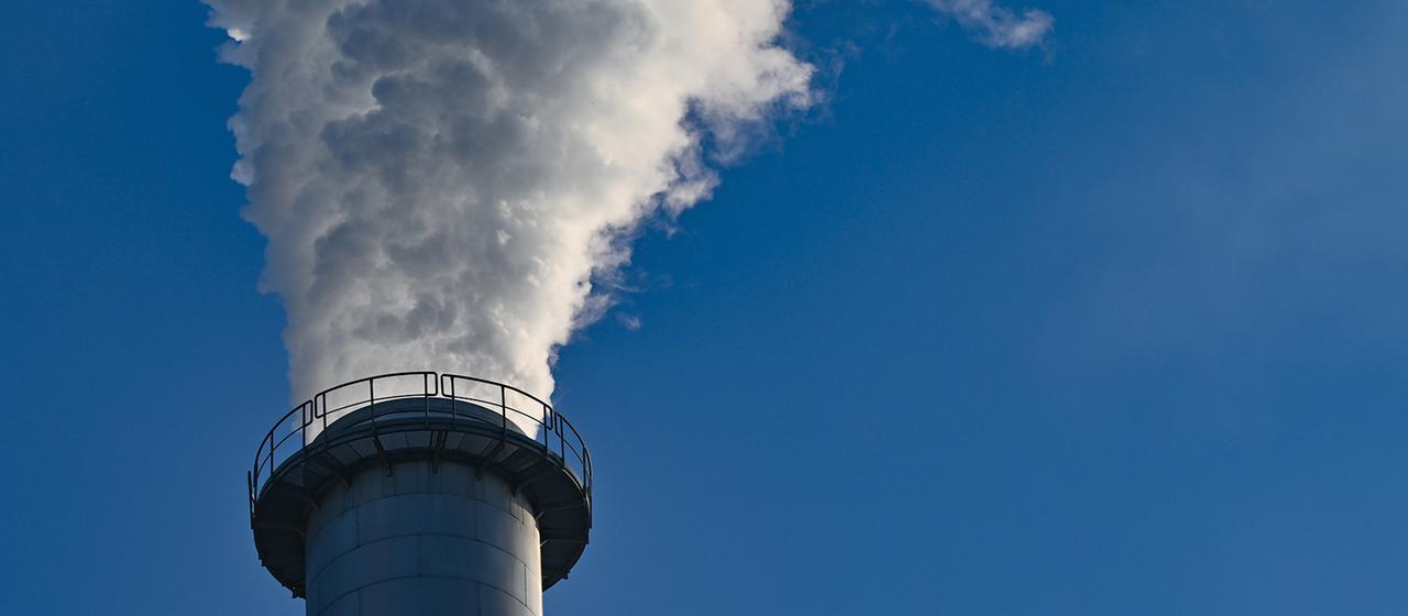 Dampf und Abgase kommen aus einem Schornstein einer Fabrik.