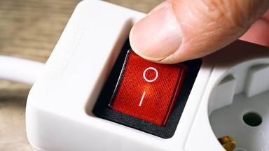 Finger schaltet Kippschalter an einer Mehrfachsteckdosenleiste aus.