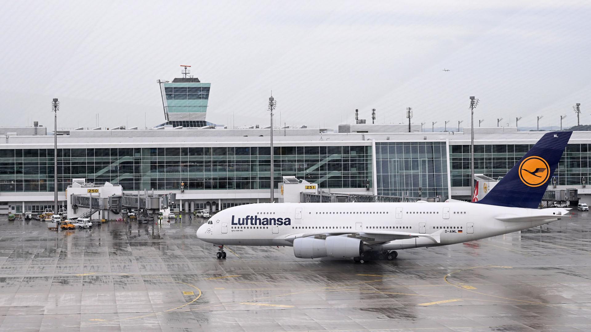 Eine Maschine der Fluggesellschaft Lufthansa rollt vor einem Tower am Flughafen München zur Standposition. | dpa