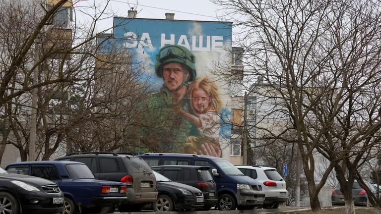 Eine Wandbemalung an einem Haus auf der besetzten Halbinsel Krim zeigt einen russischen Soldaten, der ein Mädchen trägt.