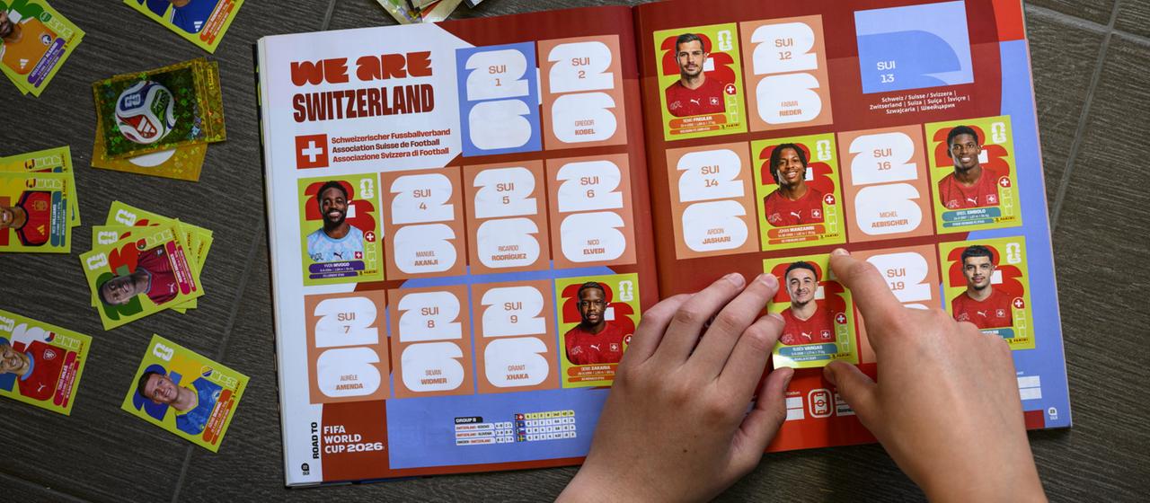 Ein Mensch klebt Panini-Sticker in das WM-Heft ein