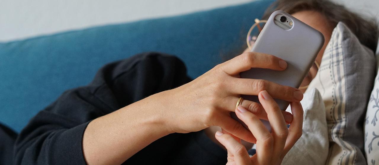 Eine junge Frau liegt auf einem Sofa und schaut auf ihr Smartphone. | picture alliance/dpa Eine junge Frau liegt auf einem Sofa und schaut auf ihr Smartphone.