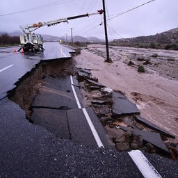 An einem Strommast neben einer teilweise weggespülten Straße finden Reparaturarbeiten statt.