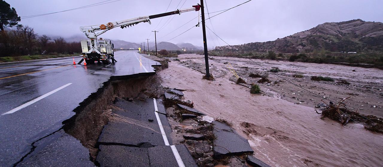 An einem Strommast neben einer teilweise weggespülten Straße finden Reparaturarbeiten statt.