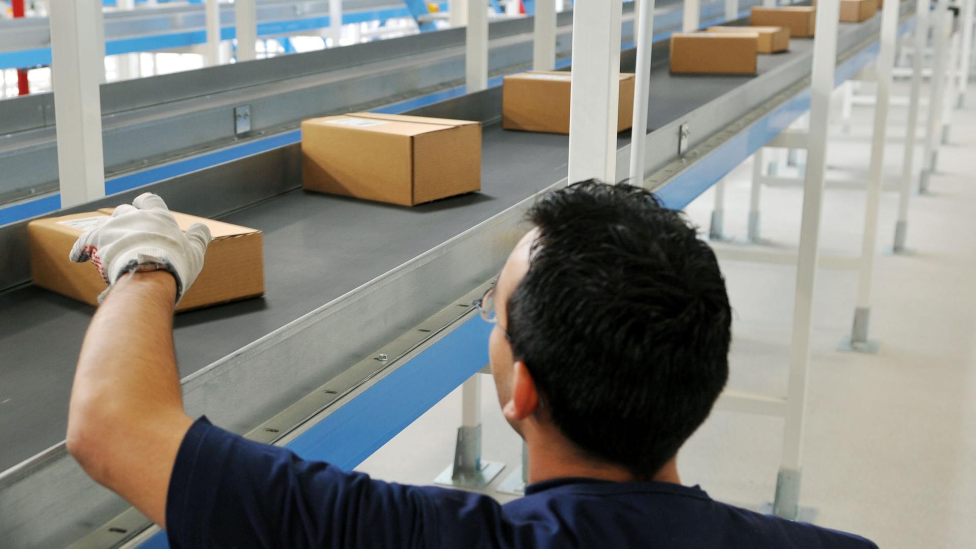 Ein Mann sortiert Pakete auf einem FlieÃband | dpa