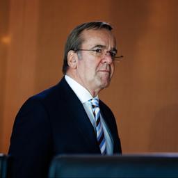 Boris Pistorius geht vor einer braunen Wand entlang.