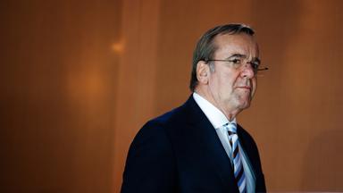 Boris Pistorius geht vor einer braunen Wand entlang.