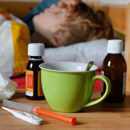 Fiebersaft, Fieberthermometer, Taschentücher und eine Tasse am Bett eines Kindes
