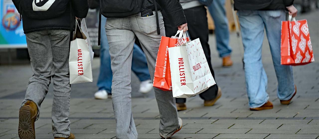 Passanten mit Einkaufstüten in einer Fußgängerzone.