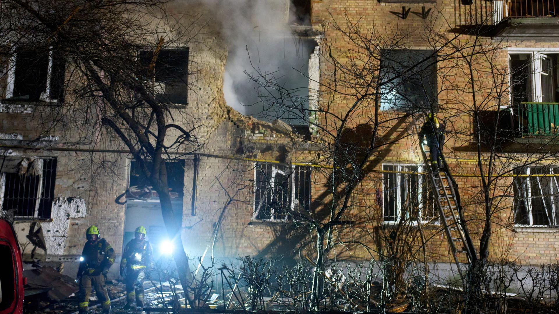 Feuerwehrleute in der Nacht vor einem zerstörten Wohnhaus in Kiew, aus dem Haus dringt Rauch. | dpa