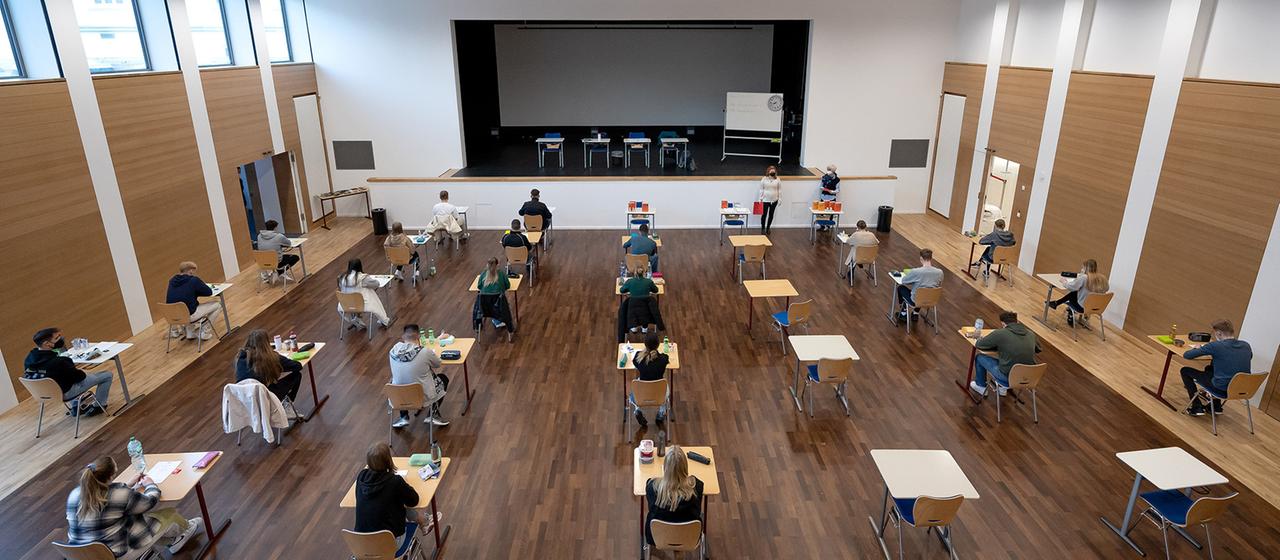 Schülerinnen und Schüler eines Gymnasiums sitzen vor Beginn ihrer schriftlichen Prüfung an ihren Plätzen.