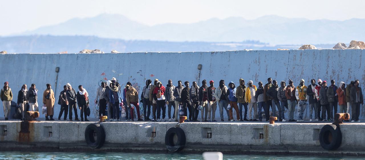 Geflüchtete Menschen stehen in einer Reihe am Hafen auf Kreta.