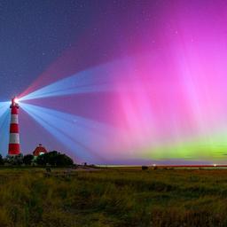 Ein rot-weiß gestreifter Leuchtturm, der in Betrieb ist, wird von violett grünen Polarlichtern angeschienen.
