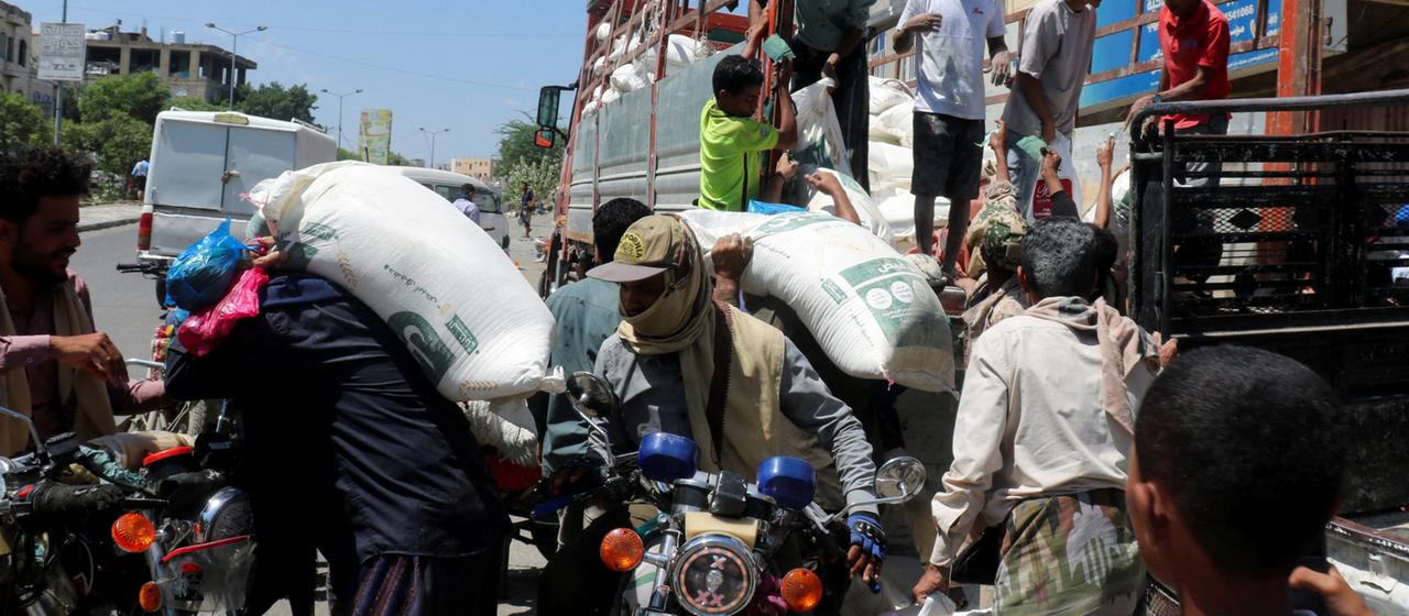 Menschen tragen Säcke mit Weizenmehl von einem geparkten Lkw in Taiz im Jemen.