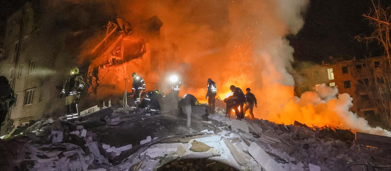 Feuerwehrleute arbeiten nachts auf den Trümmern eines eingestürzten Gebäudes.