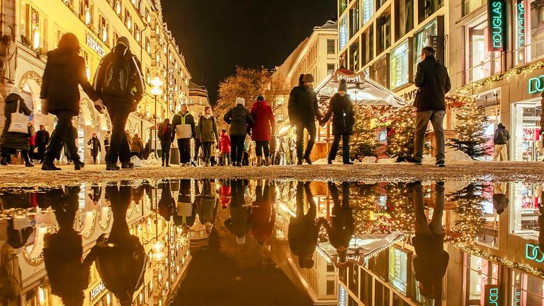 Passanten in einer weihnachtlich beleuchteten Fußgängerzone.