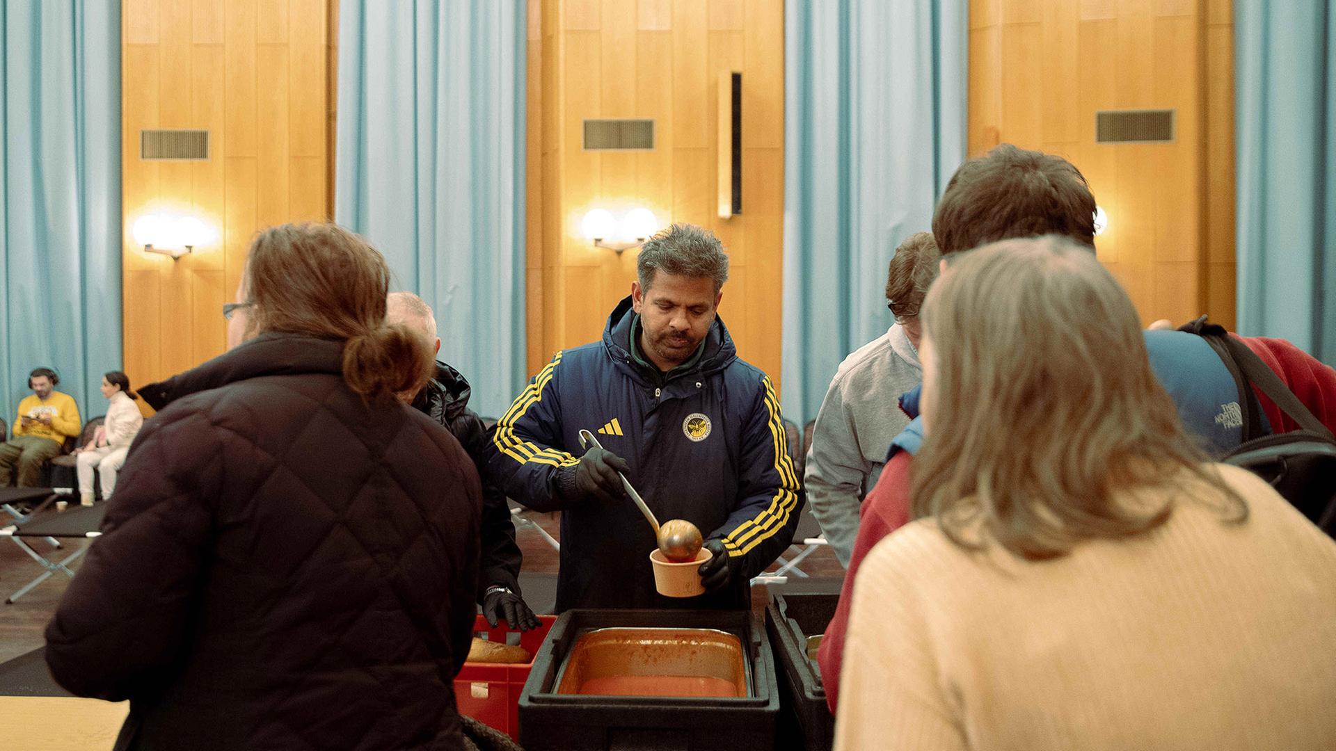 Ehrenamtliche verteilen Essen während eines Stromausfalls im Südwesten Berlins in einer Notunterkunft.(Quelle:picture alliance/dpa/C.Koall) | picture alliance/dpa/C.Koall