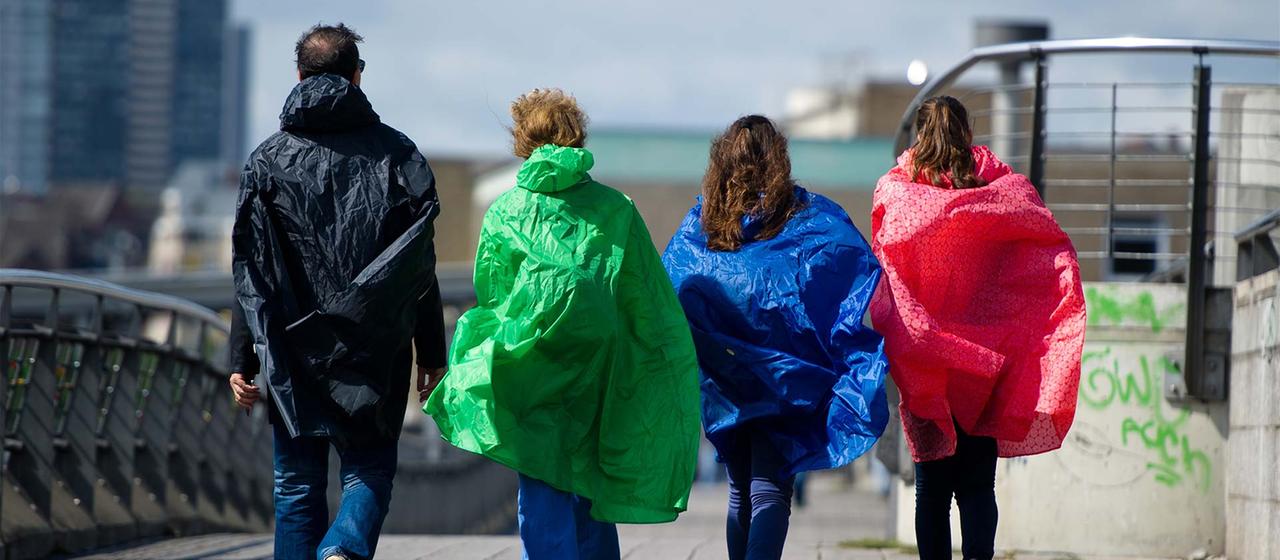 Vier Personen mit Regenjacken und -umhängen