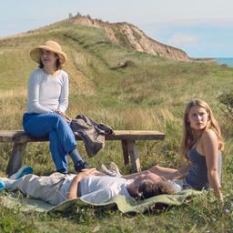 Eine dreiköpfige Familie sitzt und liegt auf einer Wiese. 