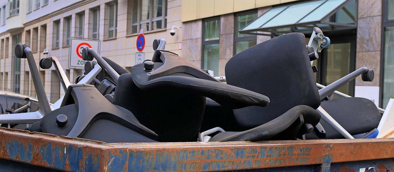 Büromöbel in einem Müllcontainer vor einem Bürogebäude.