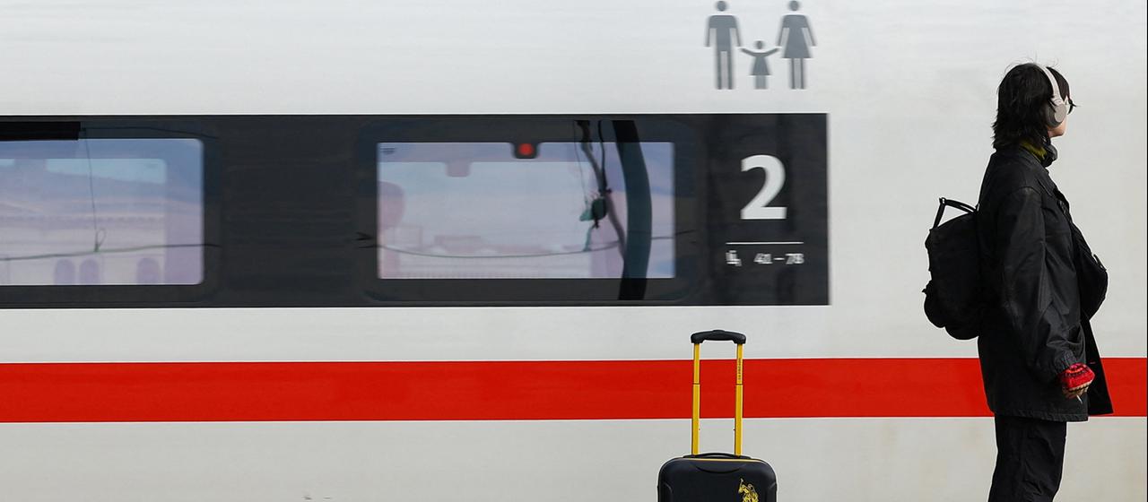Eine Frau steht mit Gepäck an einem Bahnhof