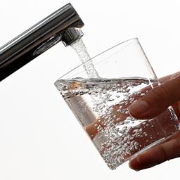 Eine Hand hält ein Glas unter einen laufenden Wasserhahn.