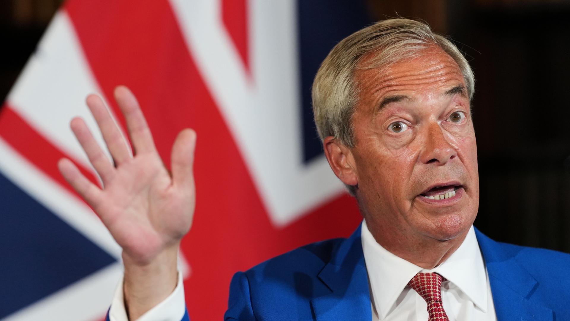 Nigel Farage mit erhobener Hand vor einem Union Jack | AP Photo/Kirsty Wigglesworth