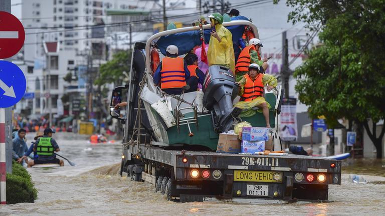 Menschen fahren auf der Ladefläche eines Lastwagens über eine überflutete Straße in Vietnam.