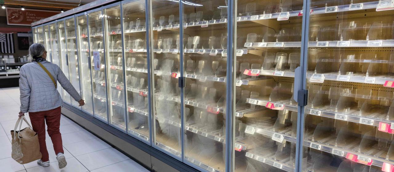 Frau vor leeren Kühlregalen in einem Supermarkt in Frankreich