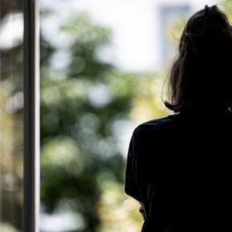 Eine Frau steht in ihrer Wohnung an einem Fenster.