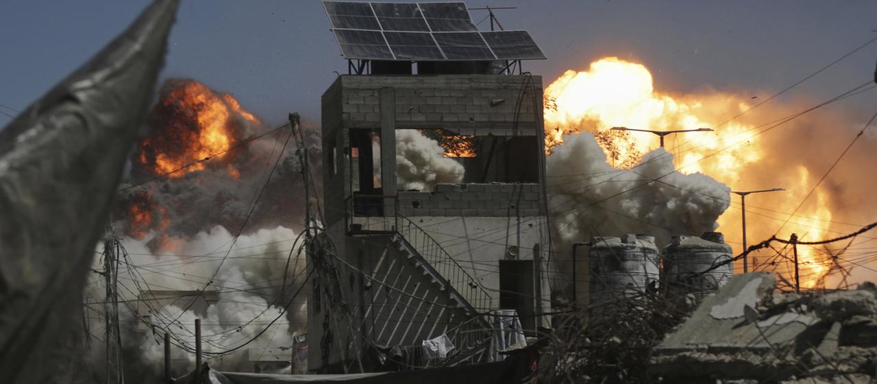 Hinter einem zerstörten Gebäude einer Stadt ist eine große Explosion zu sehen. | AP Hinter einem zerstörten Gebäude einer Stadt ist eine große Explosion zu sehen.